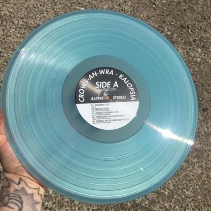 Photo of a tattooed arm and hand holding the Crows-An-Wra "Kalopsia" LP vinyl in ice v