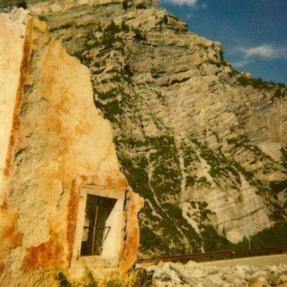 Cover of the Little Gold "On The Knife" LP. It shows a part of a sandstone wall with a window (just containing an iron cross and no glass, like a jail window) and a mountain in the background.